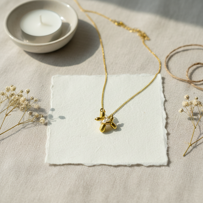 Gold necklace with a pendant on a textured surface with dried flowers and a candle.